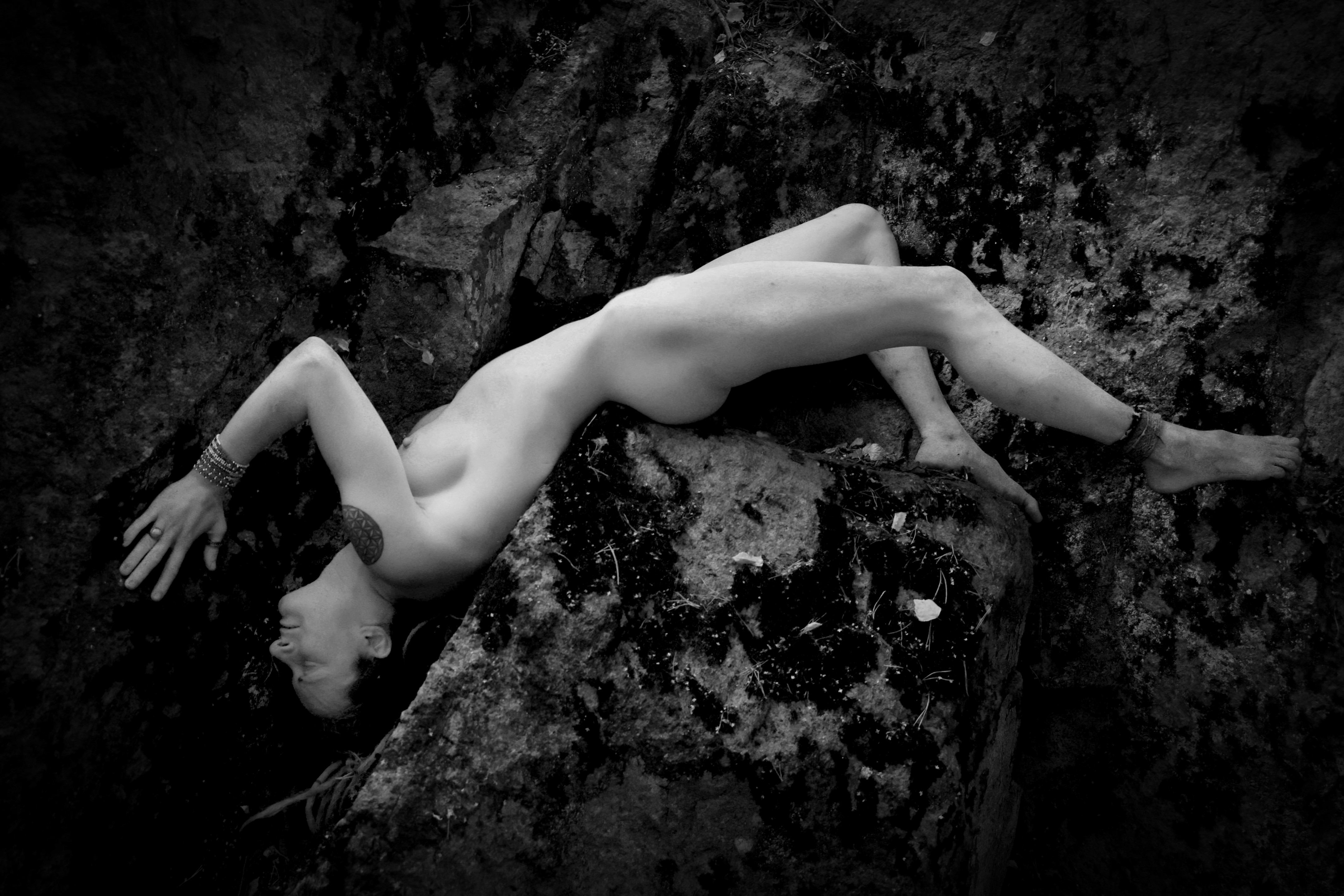 Black and white fine art nude photograph of Smirja arching her body across a large rock in a forest.