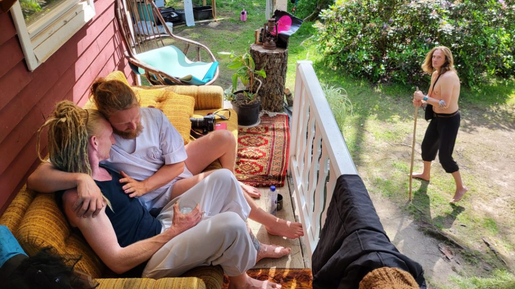 A group of naked people gathered around a fire in a forest clearing, sharing laughter, silence, and raw conversation — a moment of deep presence, honesty, and human connection at Rotum, a space where nothing is forced, and nothing needs to be explained.