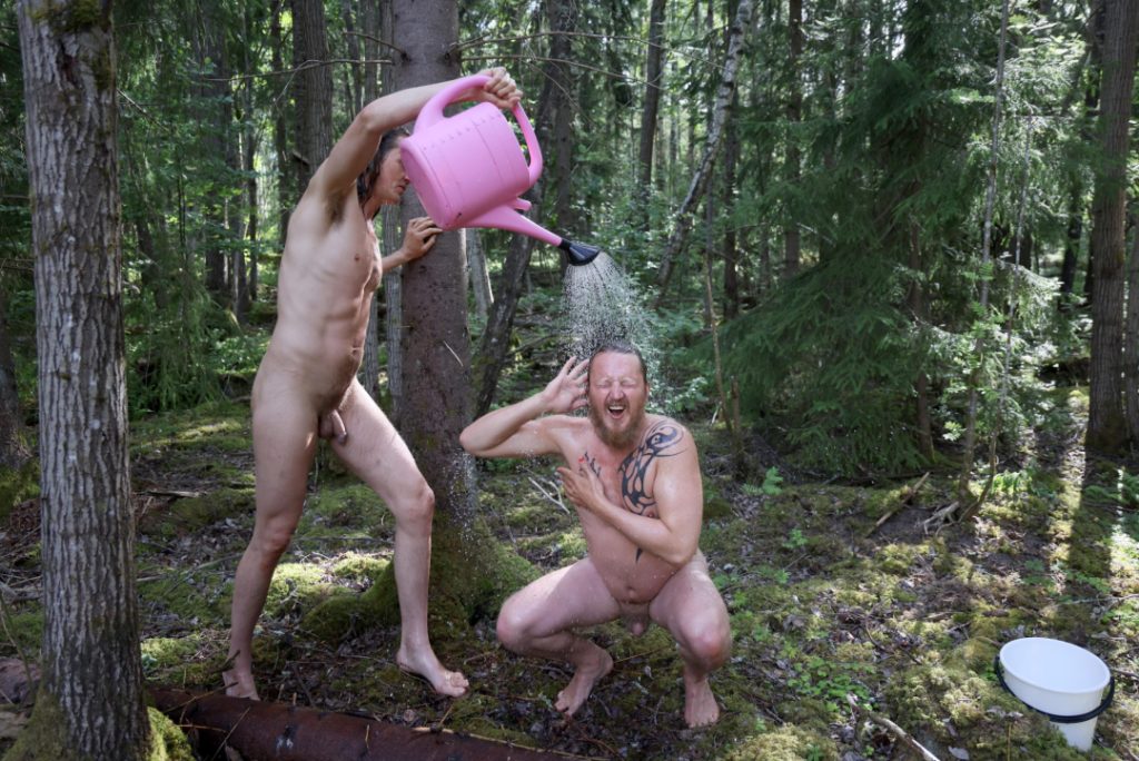 A group of naked people gathered around a fire in a forest clearing, sharing laughter, silence, and raw conversation — a moment of deep presence, honesty, and human connection at Rotum, a space where nothing is forced, and nothing needs to be explained.