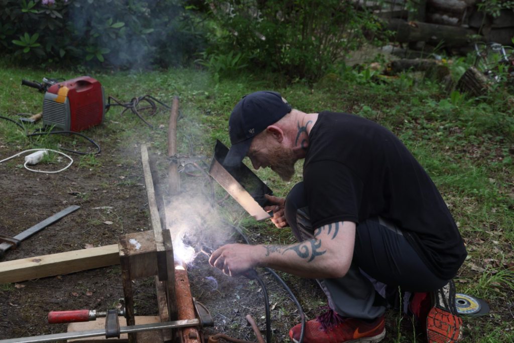 A group of naked people gathered around a fire in a forest clearing, sharing laughter, silence, and raw conversation — a moment of deep presence, honesty, and human connection at Rotum, a space where nothing is forced, and nothing needs to be explained.