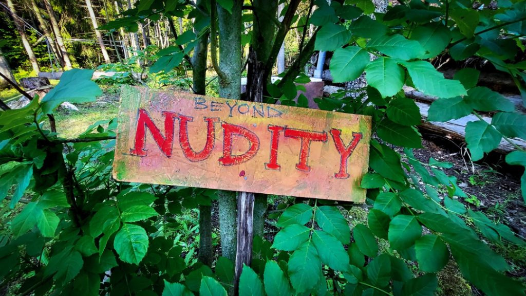 A group of naked people gathered around a fire in a forest clearing, sharing laughter, silence, and raw conversation — a moment of deep presence, honesty, and human connection at Rotum, a space where nothing is forced, and nothing needs to be explained.