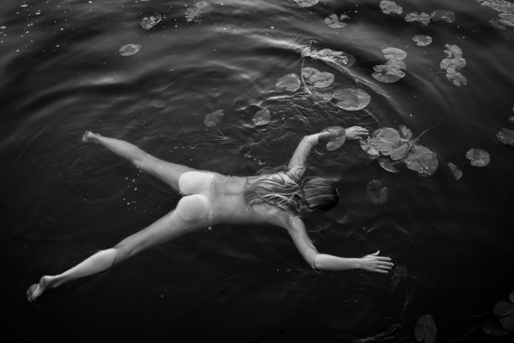The darkness of the water and the circles of the lily pads carry her form, as if she were part of the lake itself.