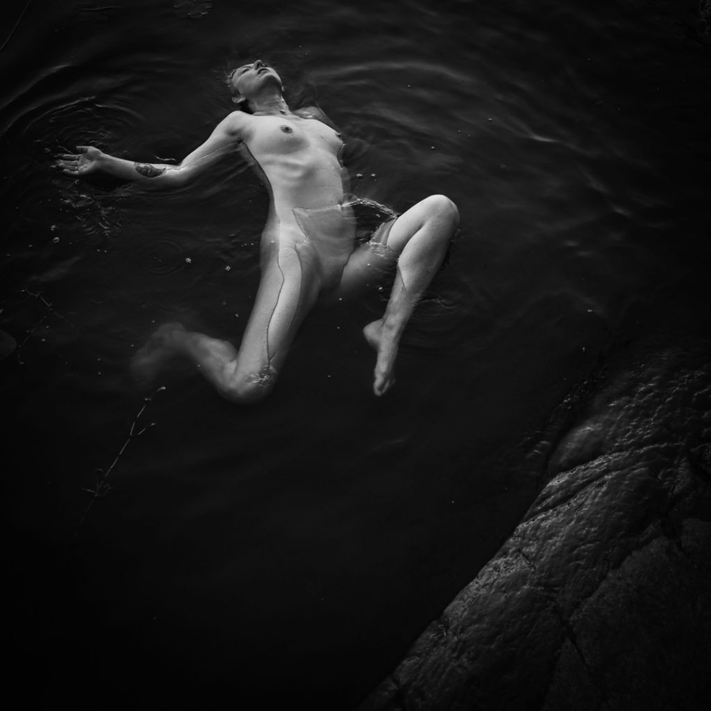 The darkness of the water and the circles of the lily pads carry her form, as if she were part of the lake itself.