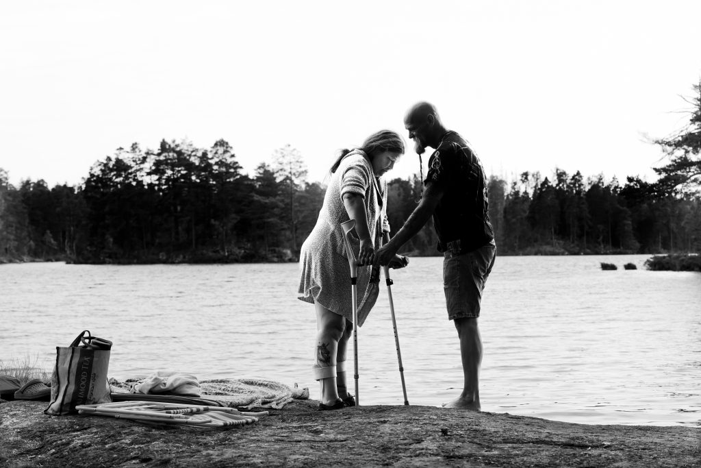 Woman on crutches receives support from man at a lake