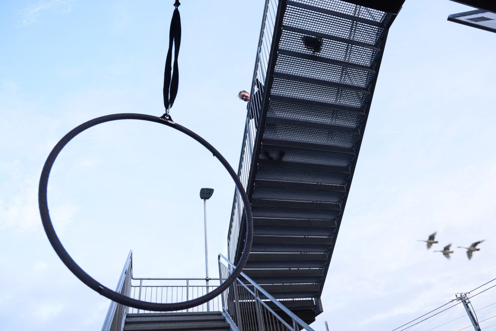 Aerial hoop suspended under a concrete bridge, with the performer holding a strong pose high above the ground in Linghem Sweden