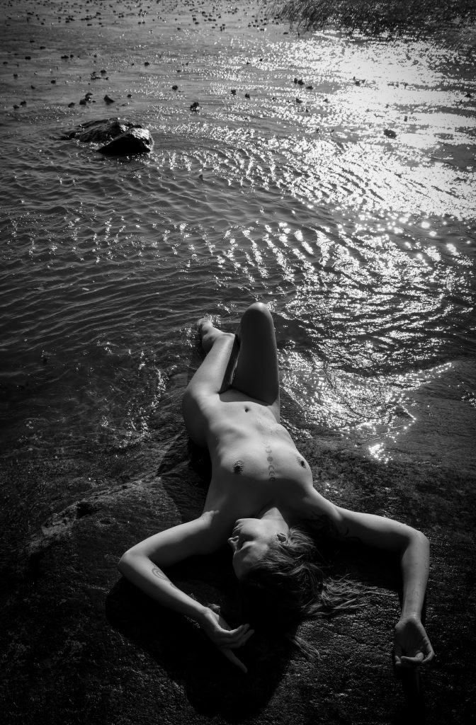 Artistic portrait of Alexandra by a calm lake, captured in natural light with a sensual and peaceful atmosphere