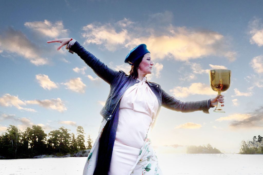 A woman stands on a frozen lake at dusk, holding a golden cup, her body poised as if performing a private ritual in the open landscape.*
